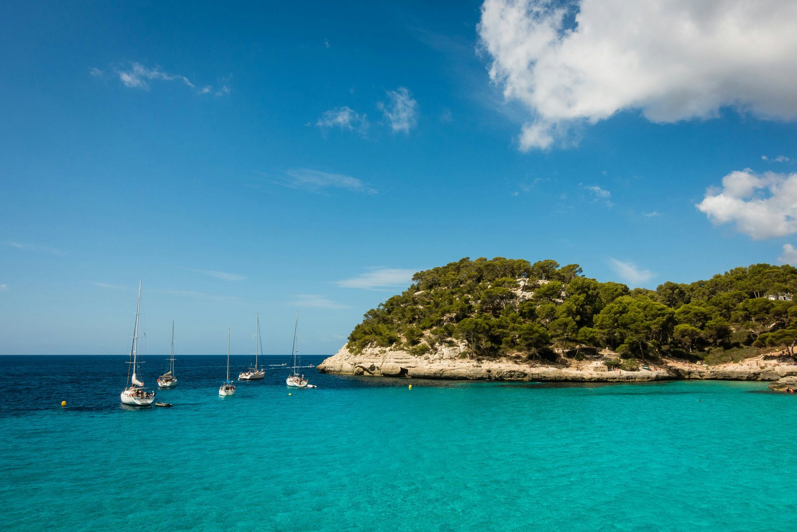 Crystal-clear cove in the Balearics with sailboats at anchor